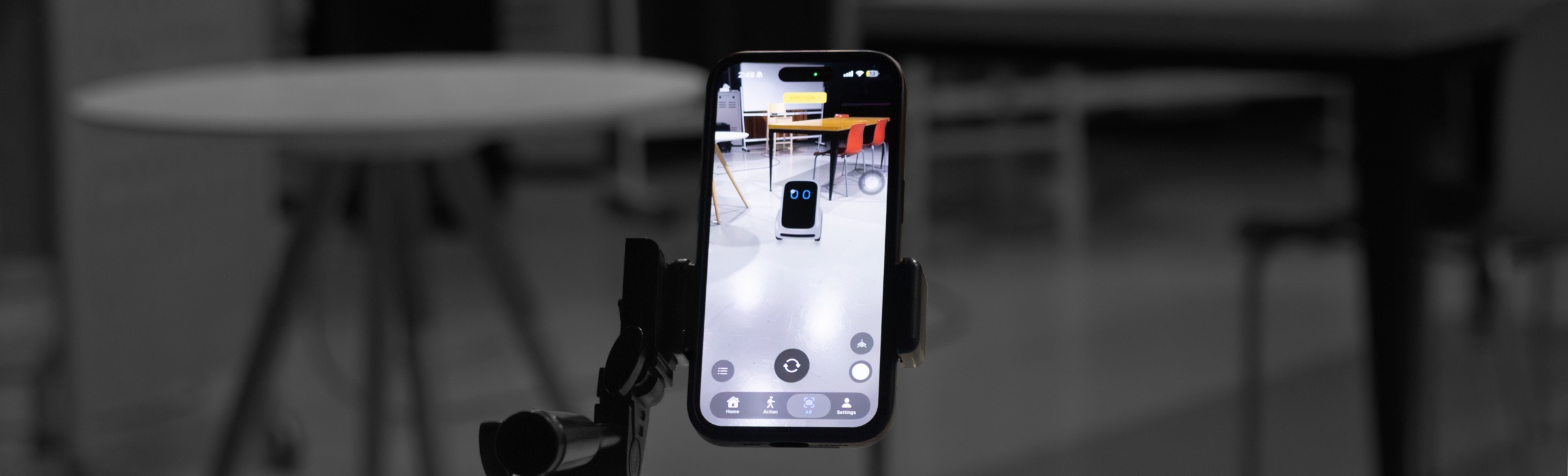 An iPhone on a tripod showing a life-size robot placed on the floor of a real room through augmented reality