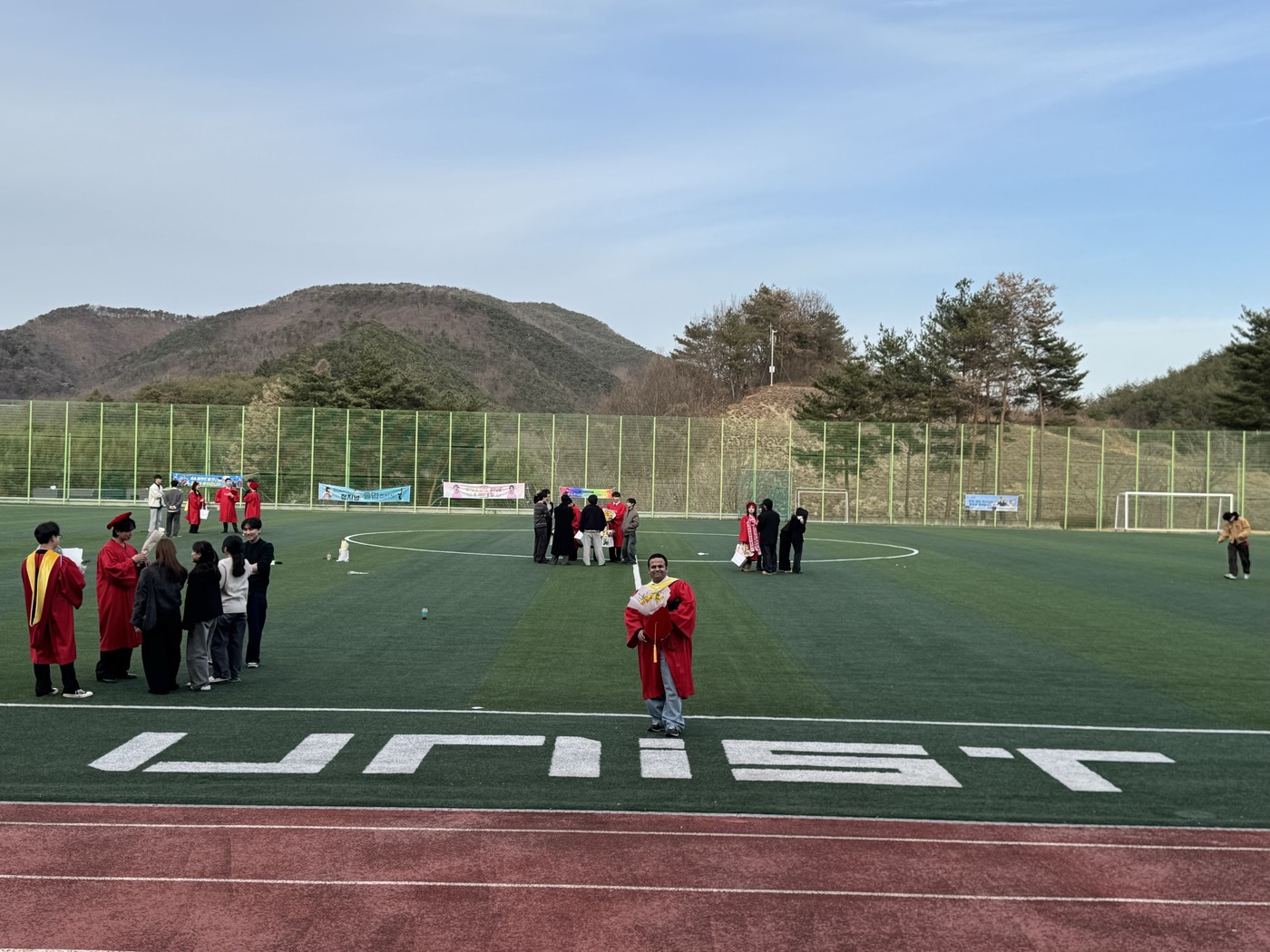 Graduates gathering on a sports field with UNIST lettering